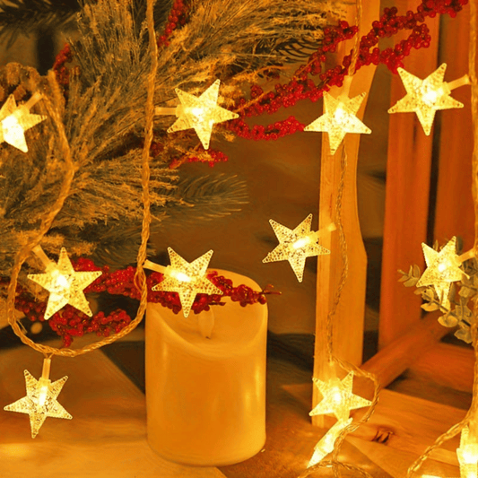 Decorative string lights shaped like stars with a candle and Christmas tree in the background.