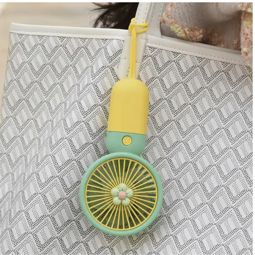 Small fan keychain with yellow top and green base on a textured surface