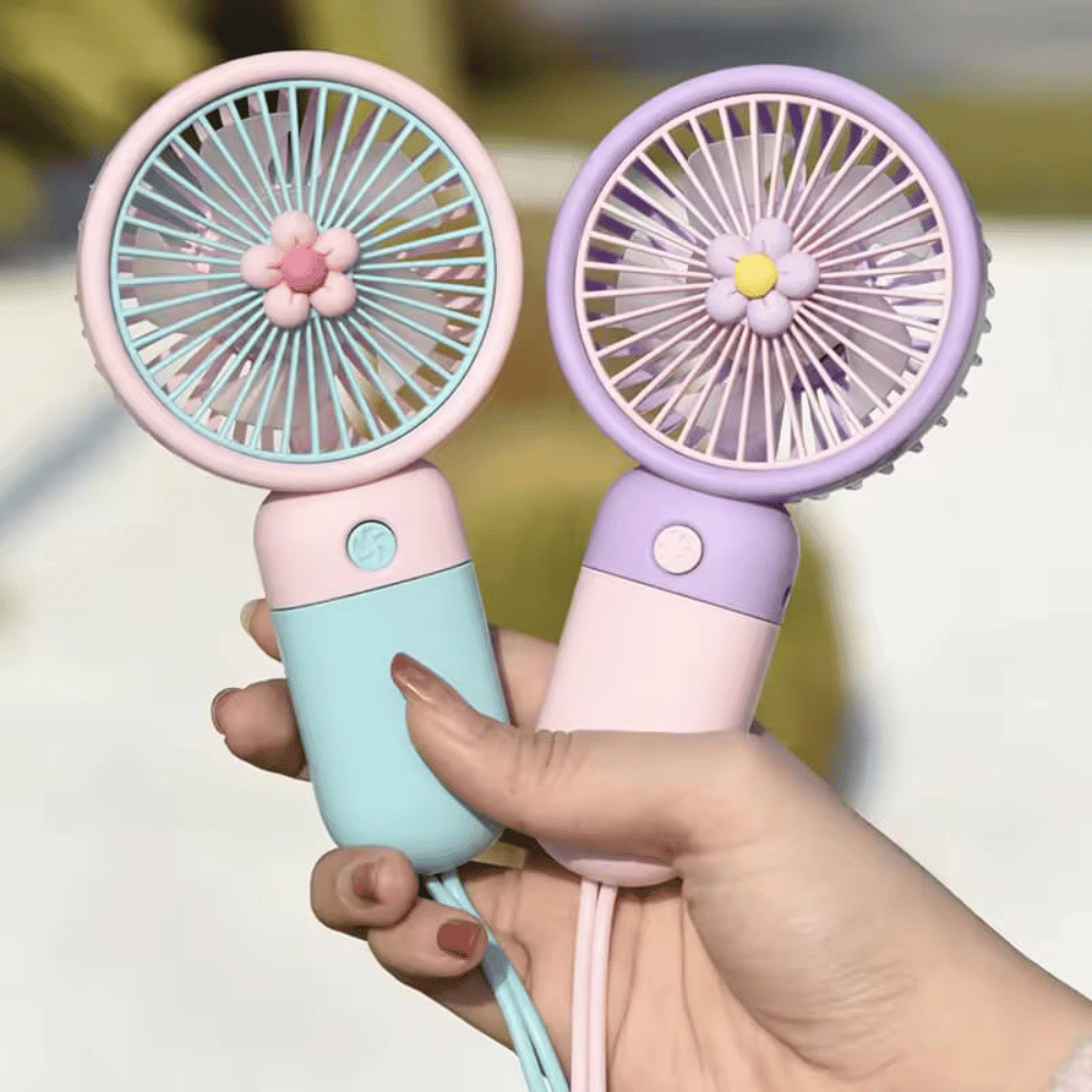 Two small handheld fans, one pink and one purple, held by a hand against a blurred background.