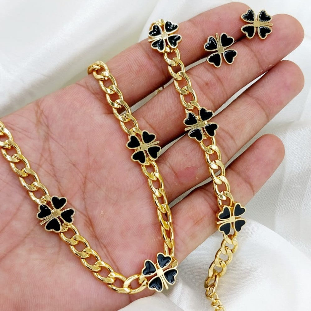 Gold chain necklace and earrings with black clover-shaped pendants on a hand.