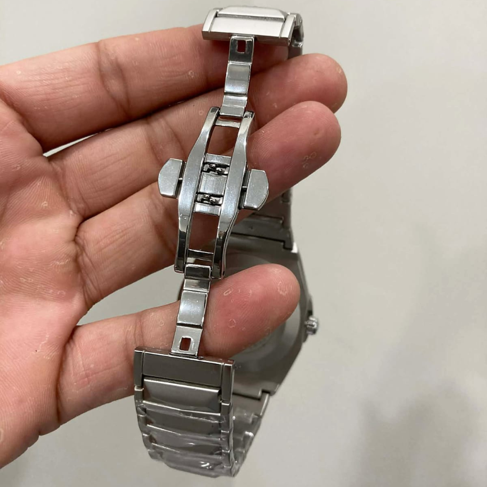 Silver watch band held in a hand against a plain background