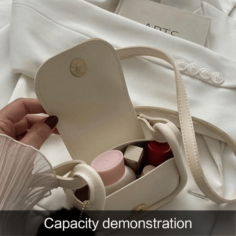 Small beige handbag with a handle, containing cosmetic items, held by a hand on a white fabric background.