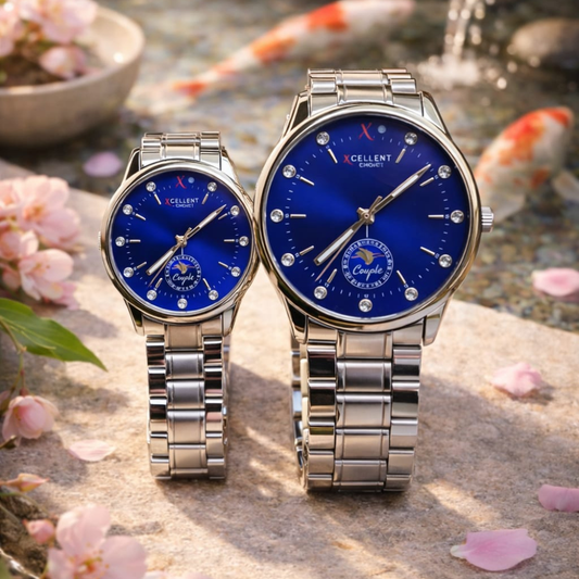 Two silver watches with blue faces on a natural background with flowers and water.