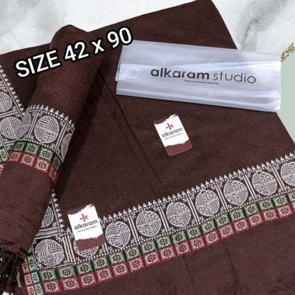 Brown fabric with decorative patterns and 'alkaram studio' branding on a white background