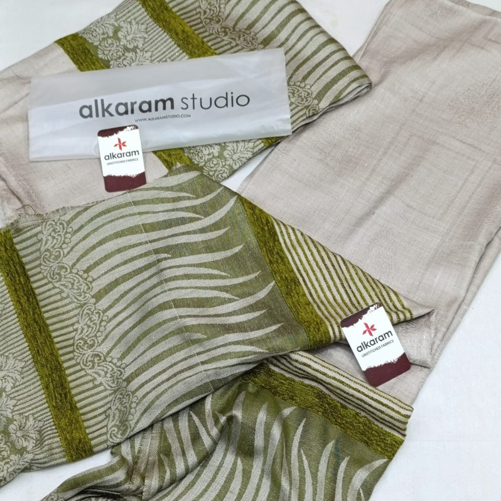 Textile with green and beige patterns and 'alkaram studio' branding.