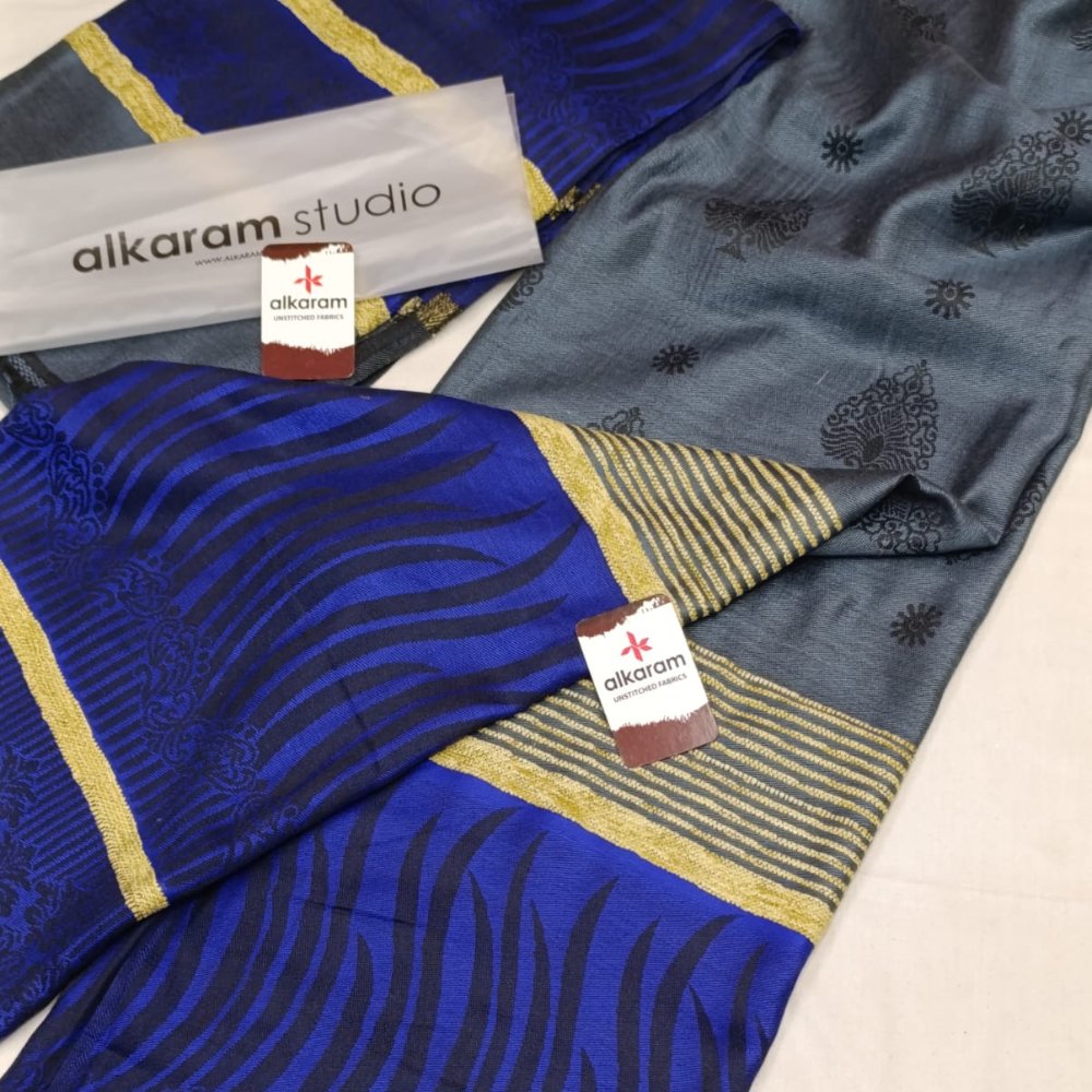 Two patterned fabrics with 'alkaram studio' branding on a white surface.