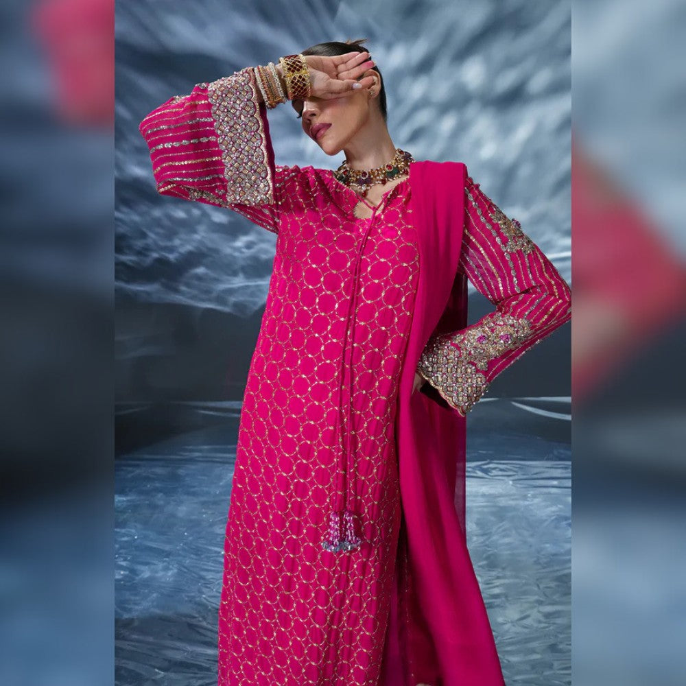 Woman in a pink traditional outfit with intricate designs against a blurred water background