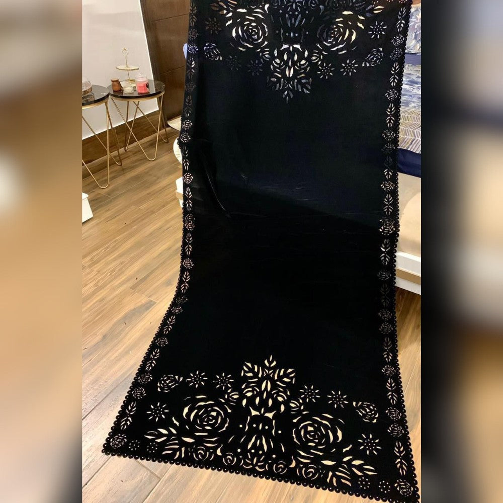 Black lace runner with floral patterns on a wooden floor.