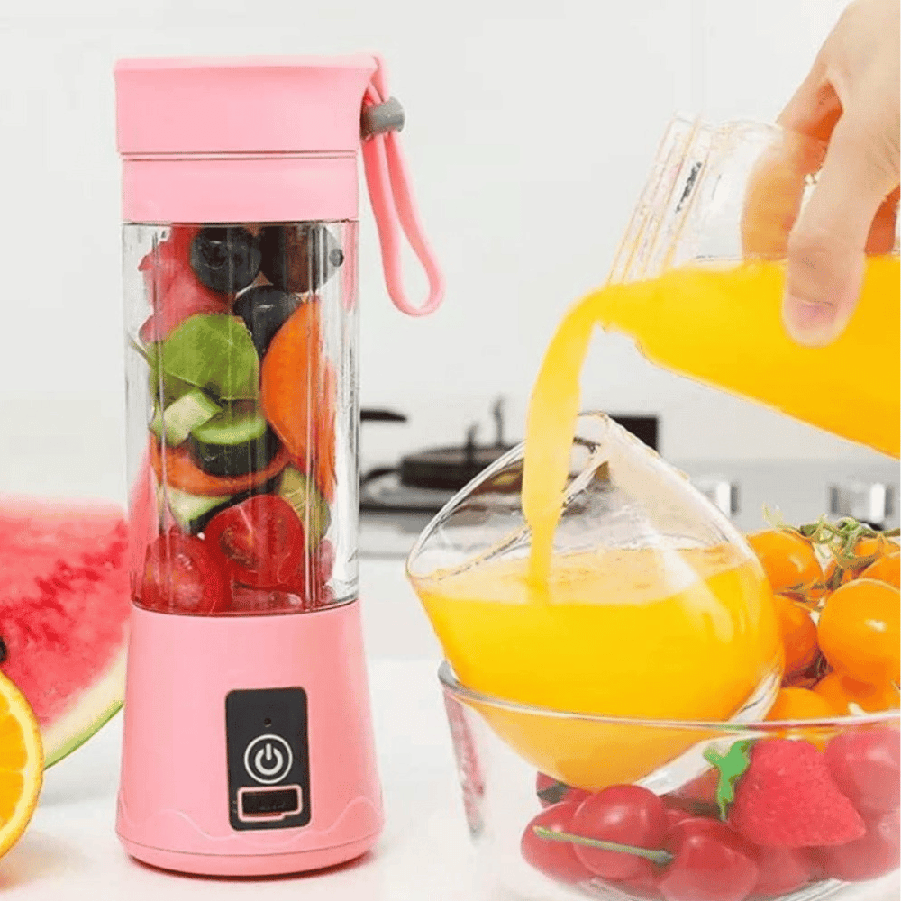 Pink portable blender with fruits inside, next to a glass of orange juice and more fruits on a white background.