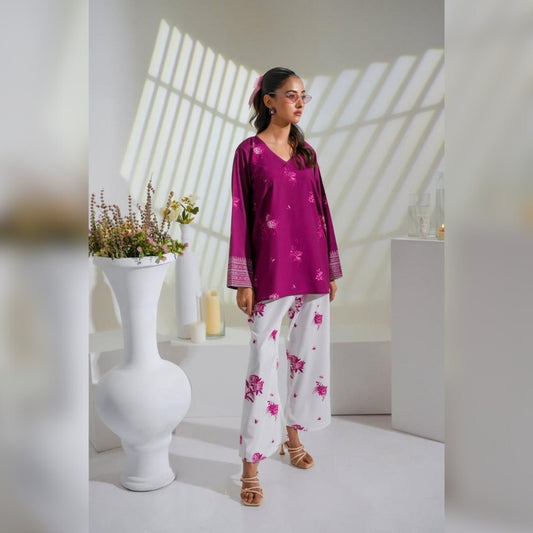 Woman in a magenta top and white pants with pink floral patterns standing in a bright room.