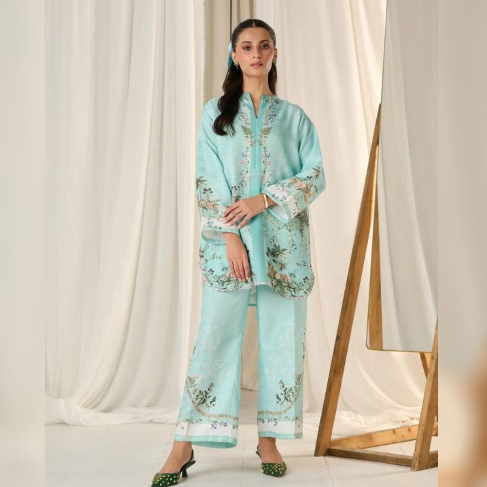 Woman wearing a light blue embroidered outfit against a white curtain background