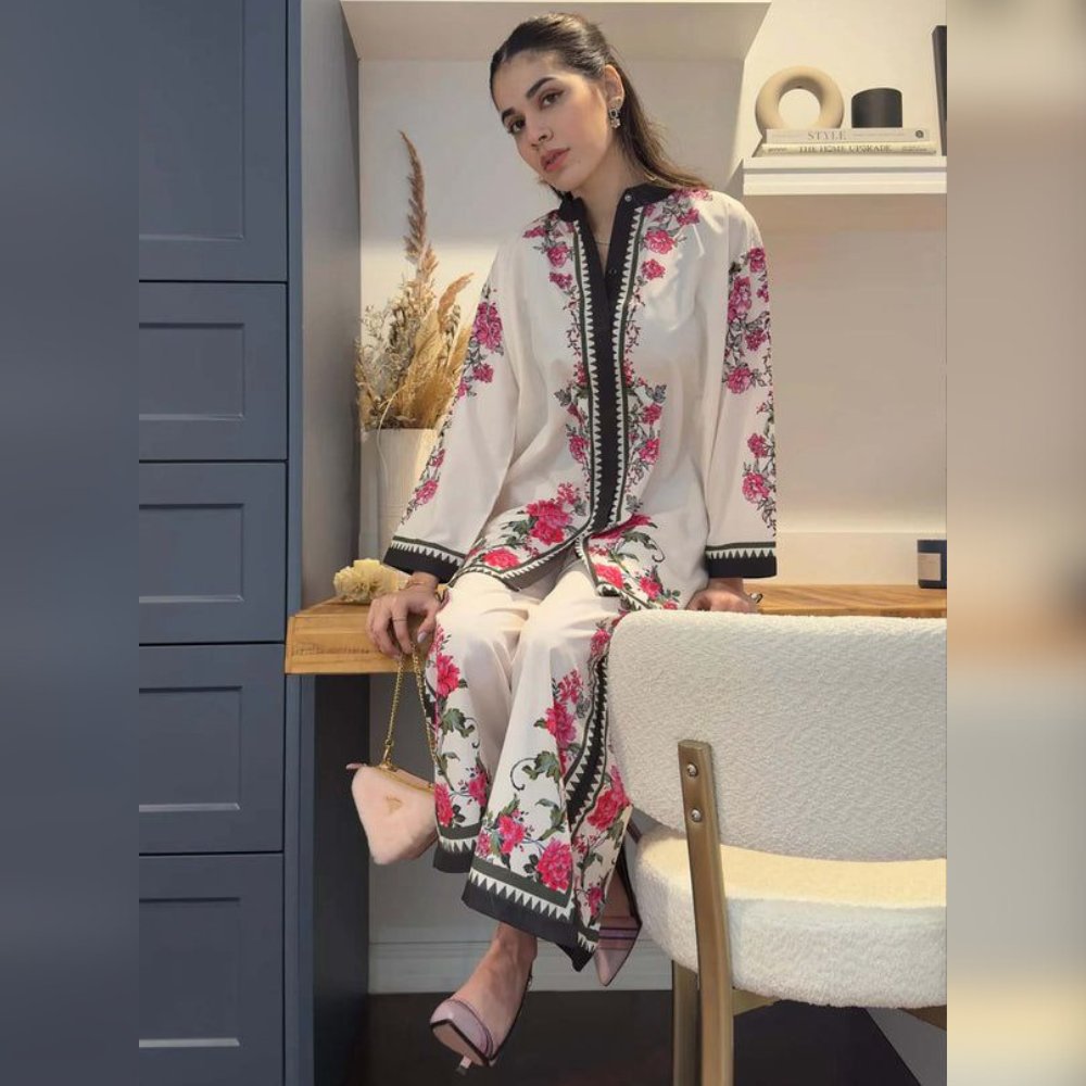 Woman in a floral embroidered outfit sitting on a chair in a room.