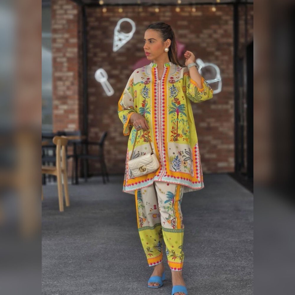 Woman in a colorful traditional outfit standing in front of a brick wall.