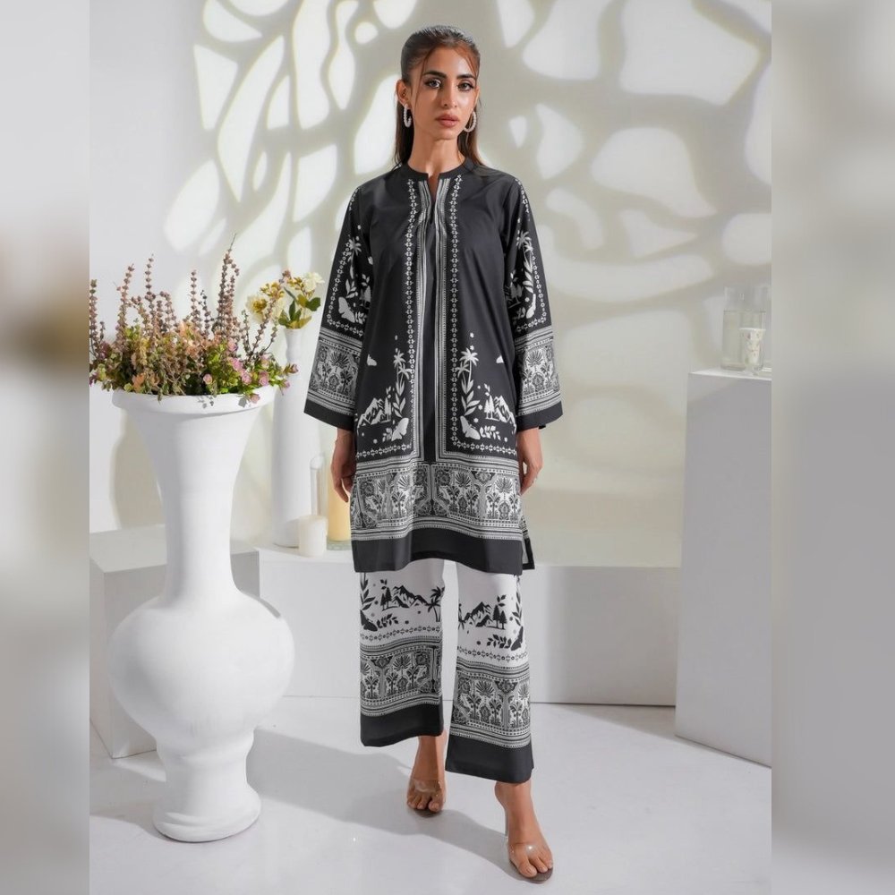 Woman wearing a black and white patterned outfit in a minimalistic setting with plants and white furniture.