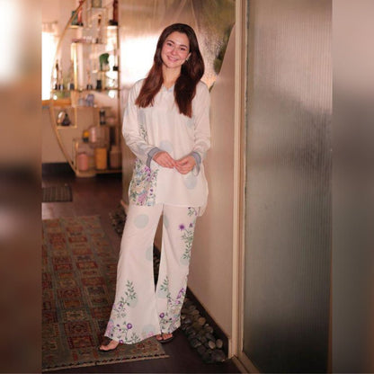Woman wearing a white outfit with floral patterns standing indoors.