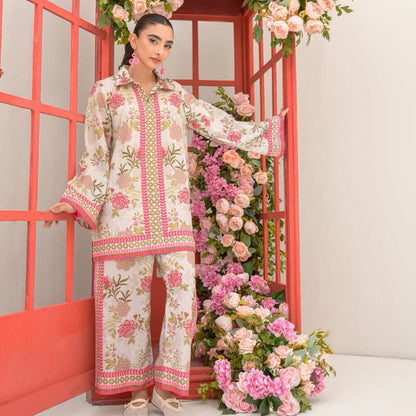 Woman in a floral embroidered outfit standing in front of a decorative floral arrangement.
