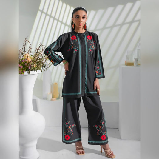Woman wearing a black embroidered outfit in a bright room with white walls and a vase of flowers.