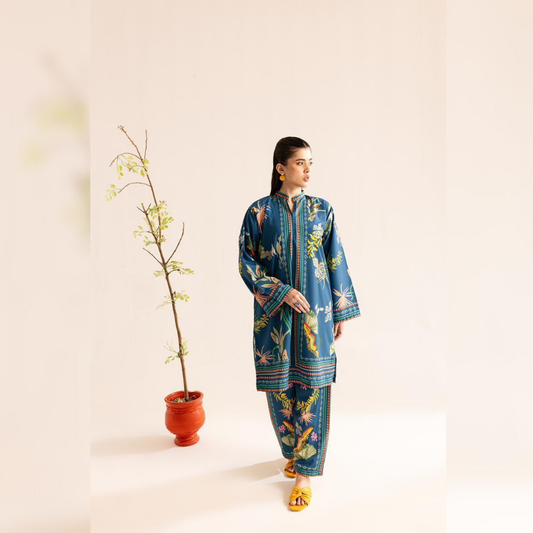 Woman wearing a blue floral traditional outfit standing next to a plant on a light background