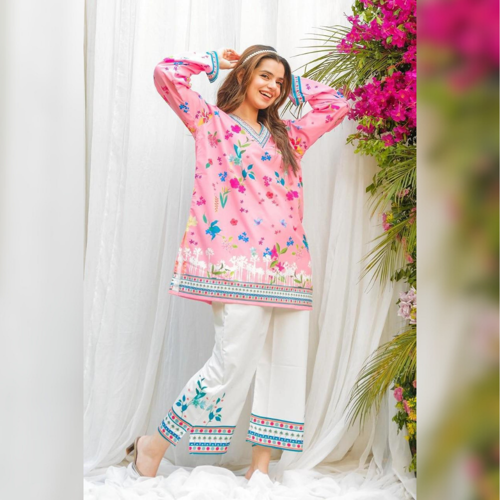 Woman wearing a pink floral dress with white pants in a decorated indoor setting.