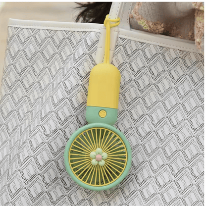 Small fan keychain with yellow top and green base on a textured surface