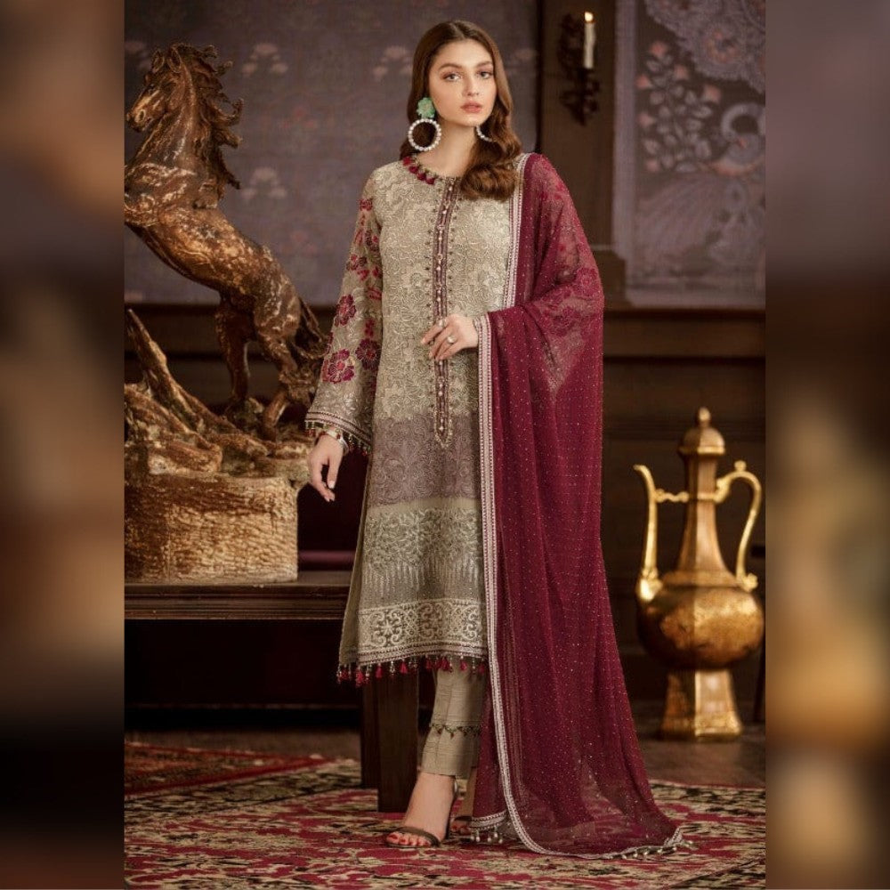 Woman in traditional embroidered outfit with a maroon dupatta in an ornate room.
