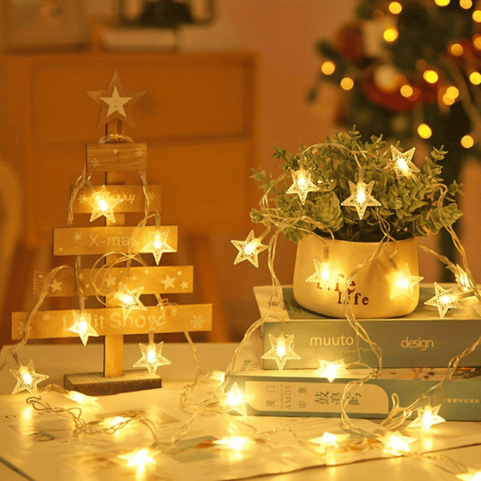Decorative setup with a wooden Christmas tree, potted plant, and string lights on a table.