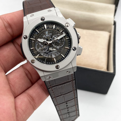 Hublot watch with brown leather strap held in a hand, with a box in the background.