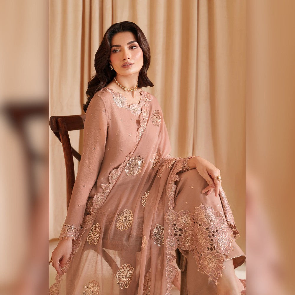 Woman in a pink embroidered traditional outfit sitting against a beige curtain.