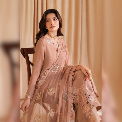 Woman in a pink embroidered traditional outfit sitting against a beige curtain.