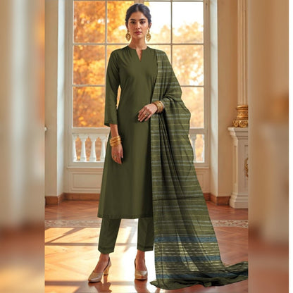 Woman wearing a green traditional outfit with a matching dupatta in a room with large windows.