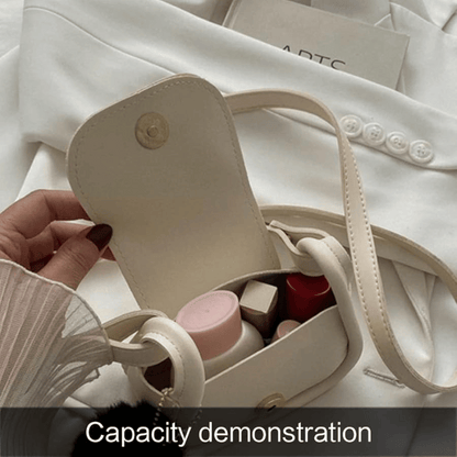Small beige handbag with a handle, containing cosmetic items, held by a hand on a white fabric background.