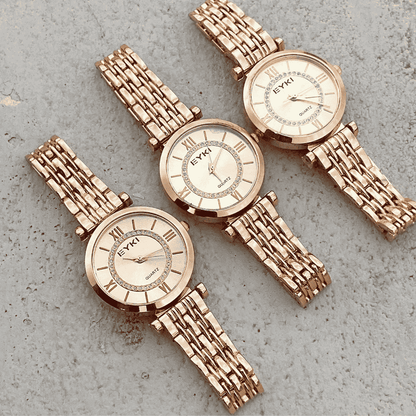 Two rose gold watches with textured bands on a gray surface
