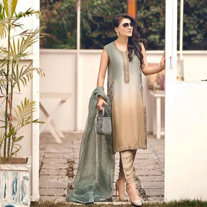 Woman in a light green and beige outfit holding a green dupatta with plants and a white wall in the background