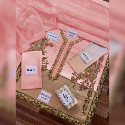 Embroidered pink and gold fabric pieces on a wooden board with labels.