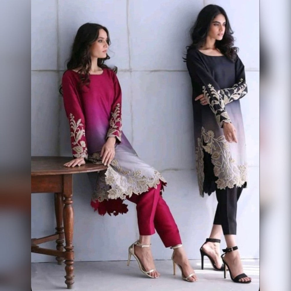 Two women wearing traditional outfits with floral embroidery against a white wall.