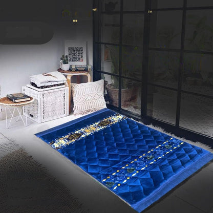 Blue prayer mat with intricate patterns on a dark floor, room setting.