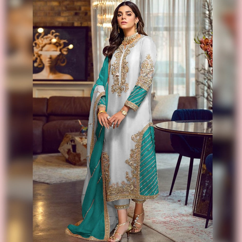 Woman in a traditional outfit with teal and gold details in a modern living room.