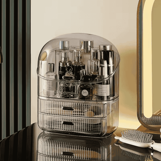 Clear cosmetic organizer with products on a reflective surface, with a mirror and decorative elements in the background.